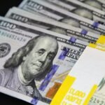 Close-up of stacked US hundred dollar bills on black surface, emphasizing wealth and finance.